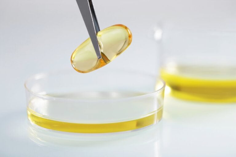 Pinzeta drží žlutou kapsli nad miskou s olejem v laboratoři
