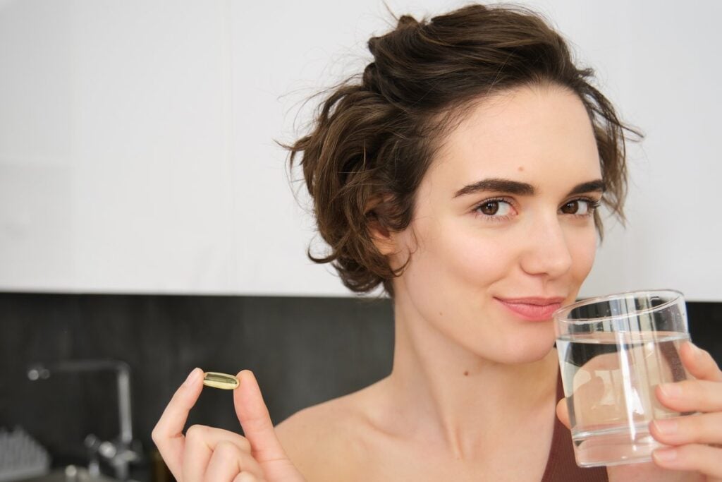 Žena v kuchyni drží kapsli omega-3 a sklenici vody