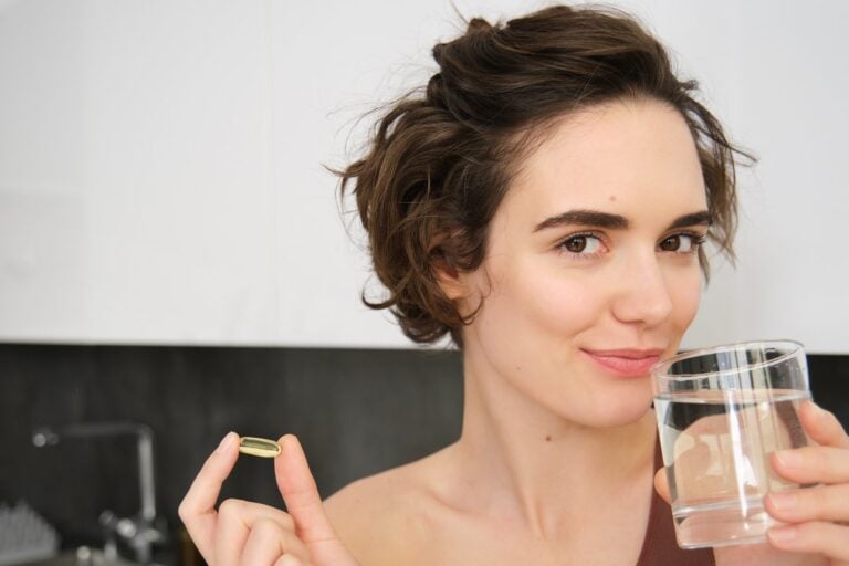 Žena v kuchyni drží kapsli omega-3 a sklenici vody